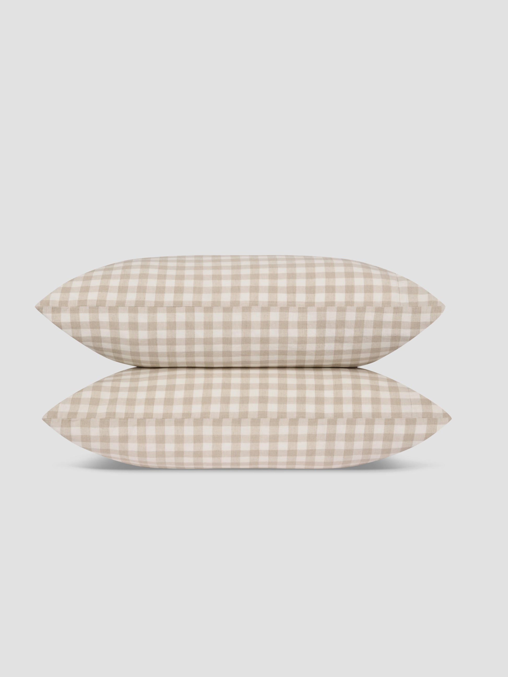 Two pillows stacked vertically, featuring a beige and off-white gingham check pattern, set against a solid light gray background.