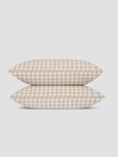 Two pillows stacked vertically, featuring a beige and off-white gingham check pattern, set against a solid light gray background.