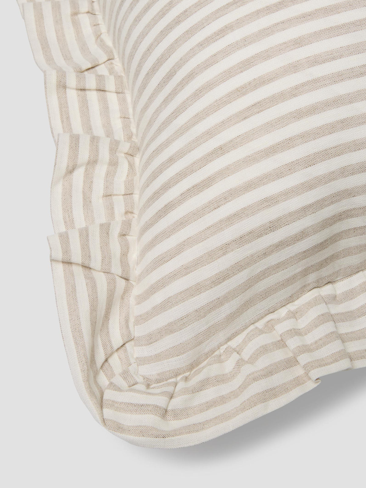Close up of an oatmeal stripe cushion with a frilled edge, on a light gray background.