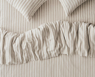 Striped bedding set with two matching pillowcases and a ruffled duvet cover in a warm beige and off-white color combination.
