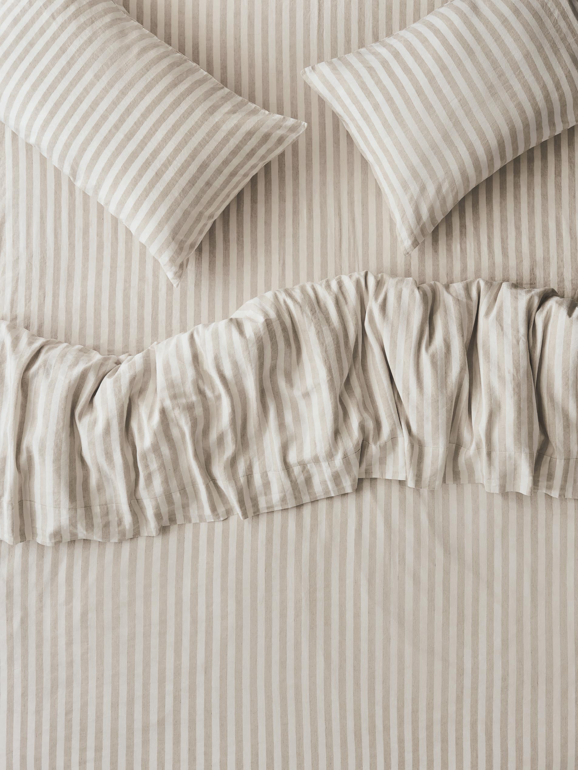 Striped bedding set with two matching pillowcases and a ruffled duvet cover in a warm beige and off-white color combination.