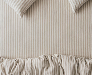 Beige and white vertically striped bedding set featuring a ruffled duvet cover and two matching striped pillows.