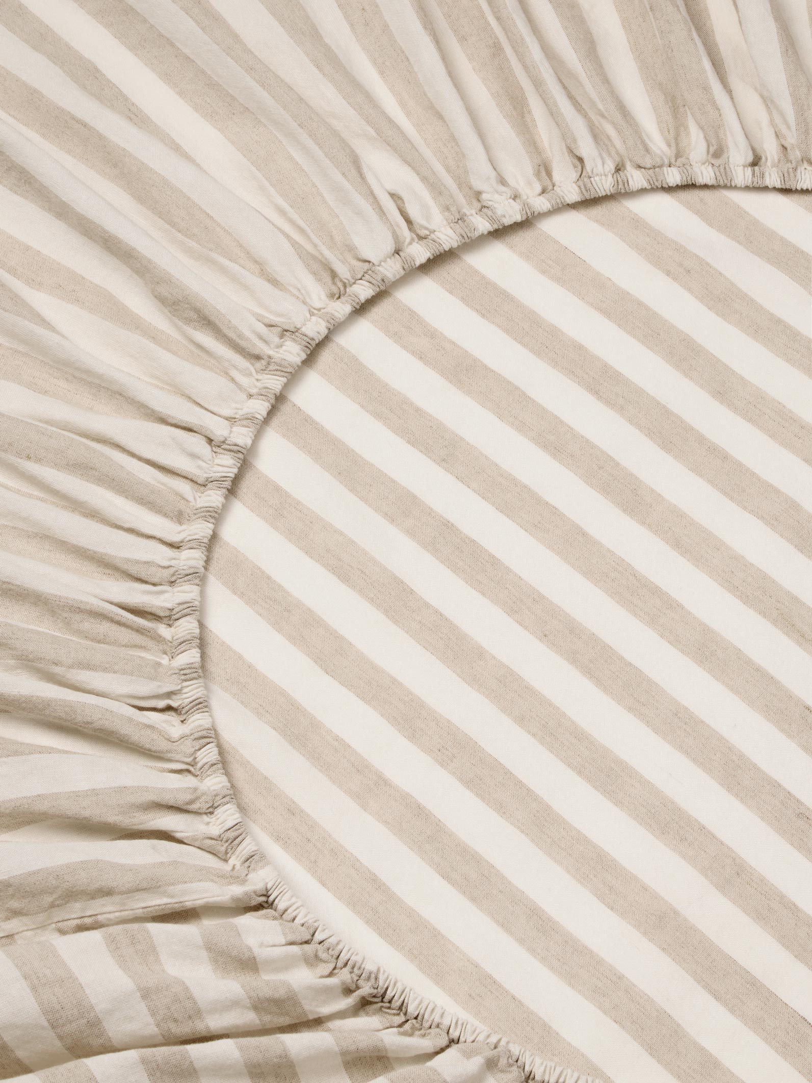 Close-up of a striped bedding fabric with a gathered elasticized edge, showing alternating warm beige and off-white diagonal stripes.