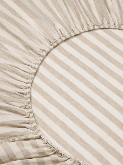 Close-up of a striped bedding fabric with a gathered elasticized edge, showing alternating warm beige and off-white diagonal stripes.