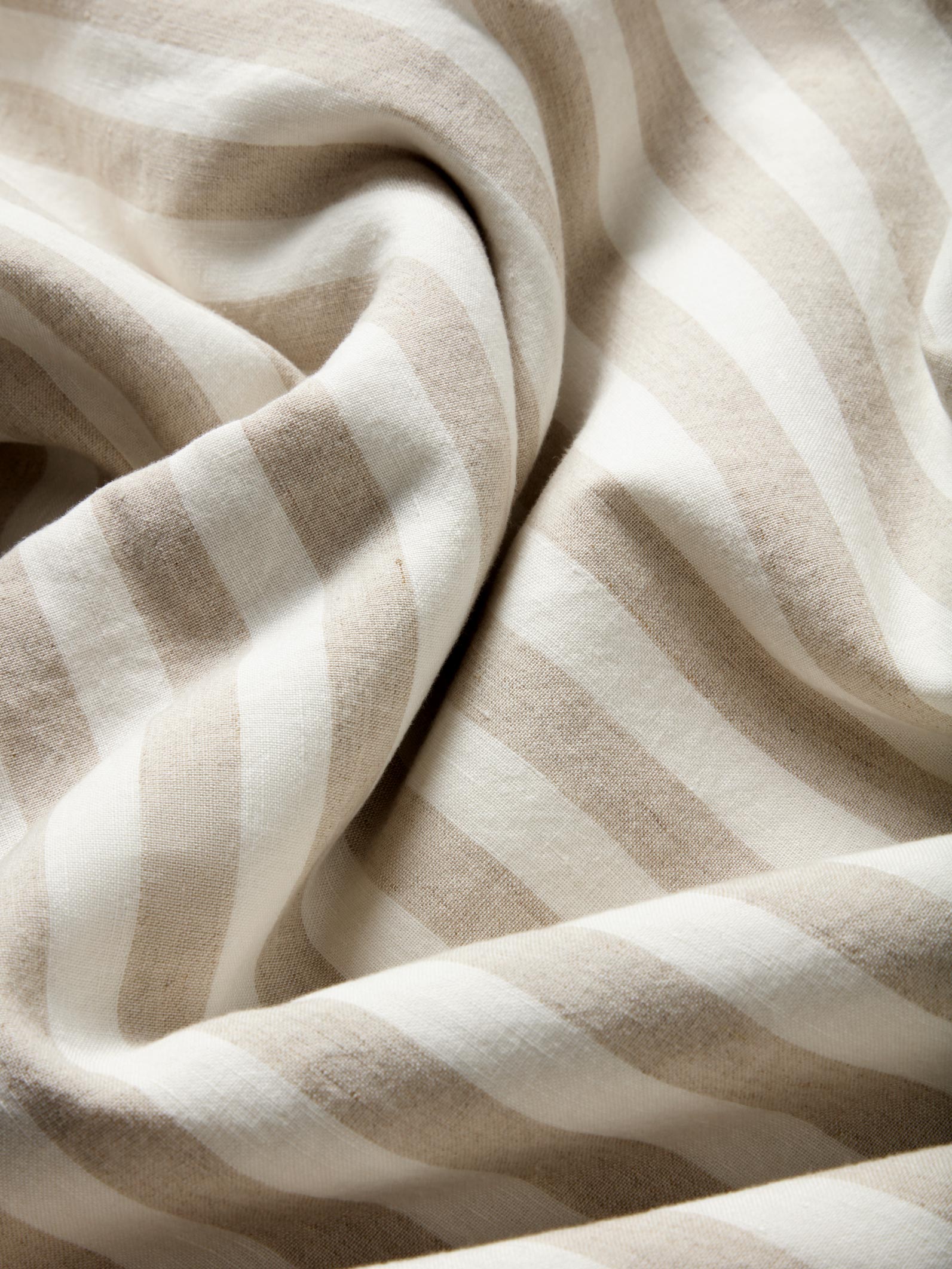 A close-up of draped fabric with soft vertical stripes in warm beige and off-white.