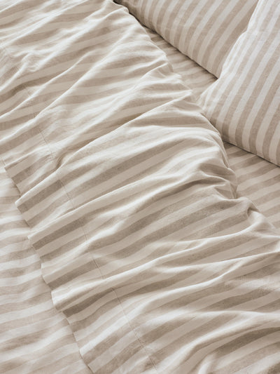 Close-up of striped bedding in warm beige and off-white tones, showing rumpled fabric and part of a matching pillow.