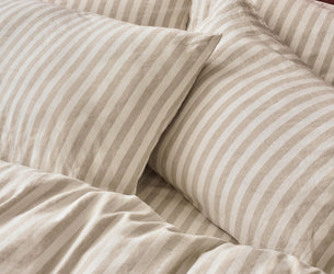 Striped bedding set with two beige and off-white striped pillowcases and matching duvet cover, styled against a dark red headboard.