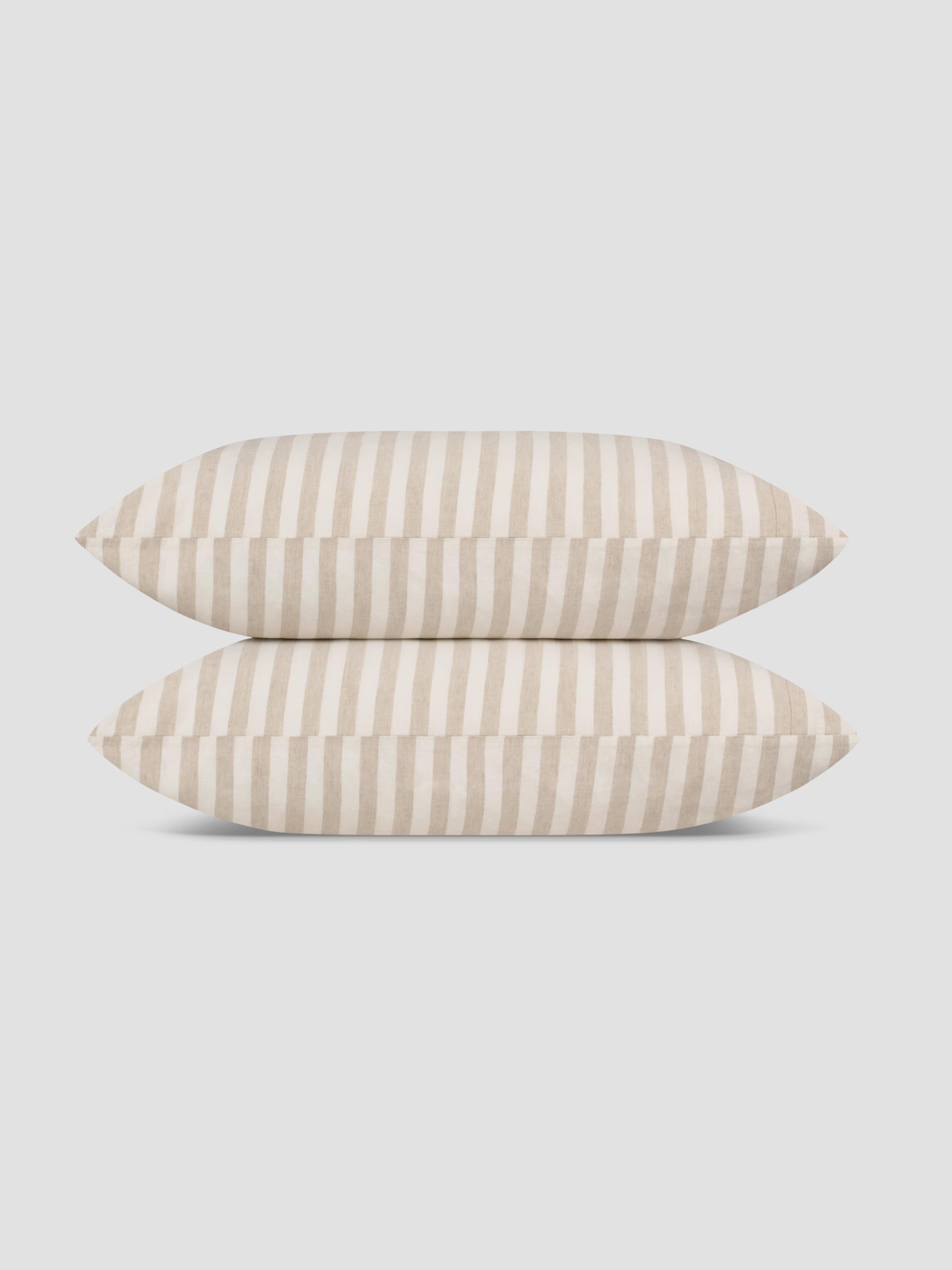 Two pillows stacked vertically, featuring a vertical stripe pattern in cream and light beige, set against a solid light gray background.