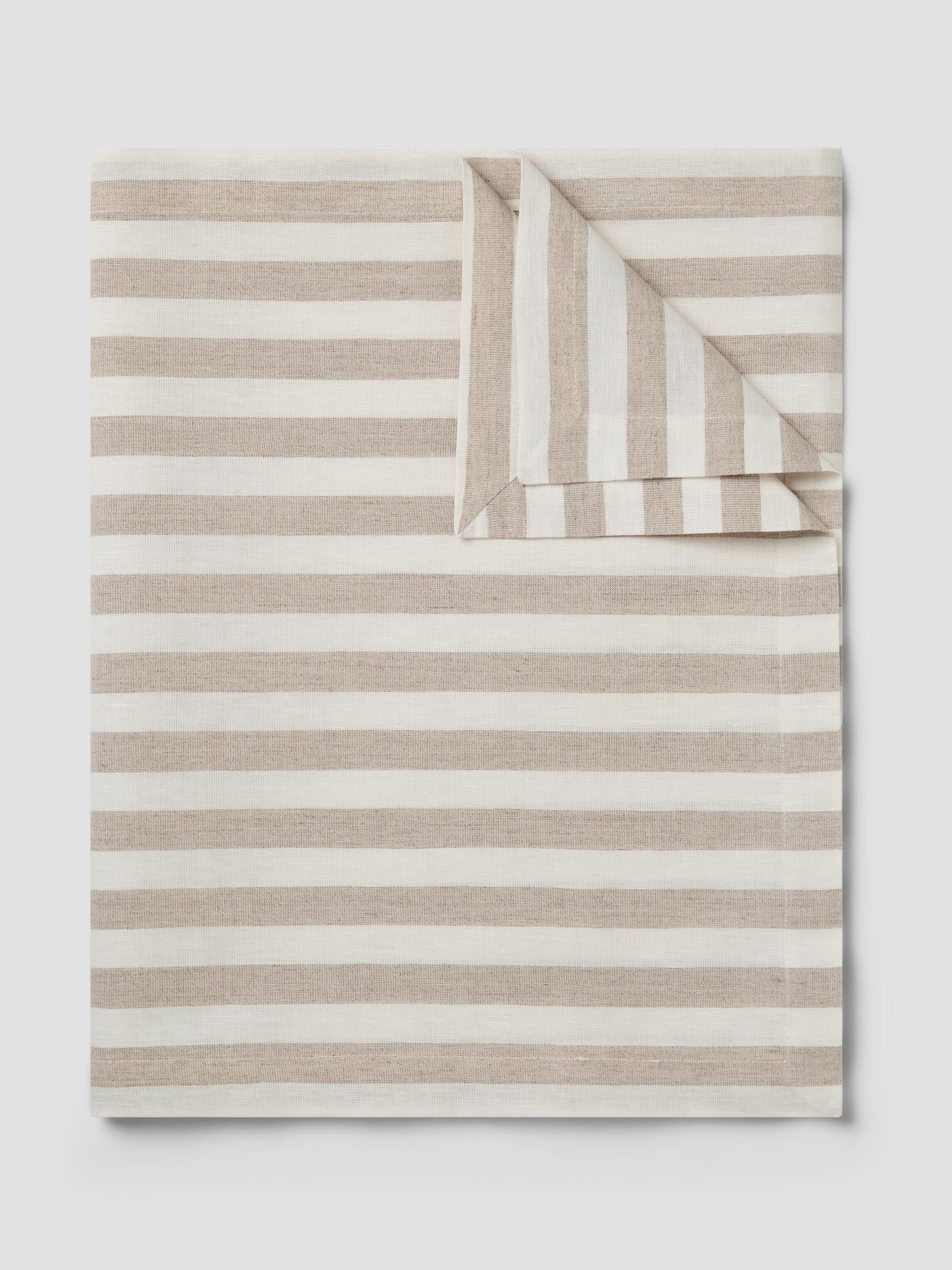 A folded striped table runner, featuring horizontal beige and off-white stripes with one corner folded over, shown on a light gray background.