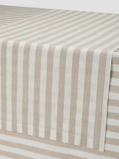 A close-up of a striped fabric table runner draped over the corner of a table, featuring alternating vertical stripes in beige and off-white.