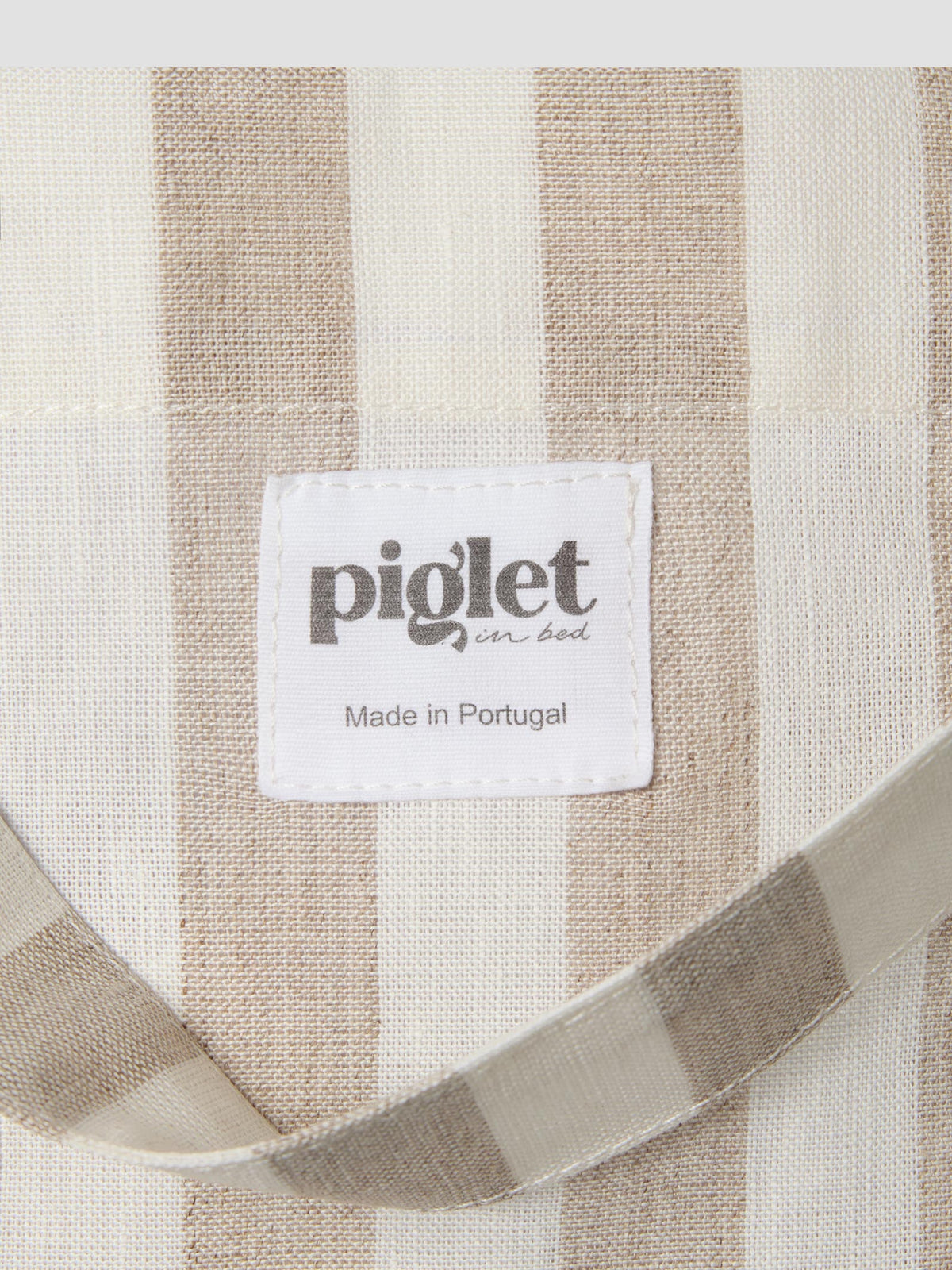 Close up of an oatmeal and white striped tote bag with a white label reading "Piglet in bed, Made in Portugal".
