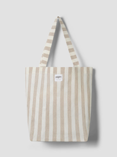 An oatmeal and white striped tote bag with a white label reading "Piglet in bed" on a light grey background.