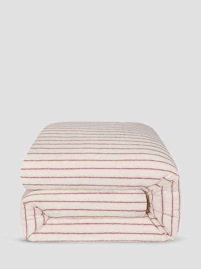 A folded comforter with thin red horizontal stripes on a cream background, shown against a solid light gray background.
