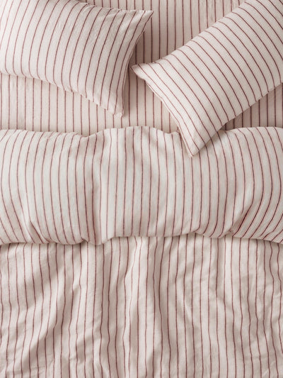 A close-up of a bedding set featuring a duvet cover and two pillows with a vertical stripe pattern in dusty pink and cream.