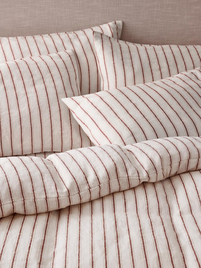 Striped bedding set with matching pillowcases and duvet cover in a warm beige fabric with thin vertical rust-red stripes.