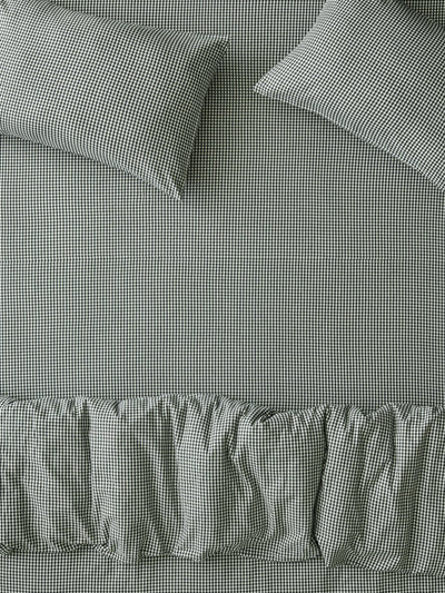 A close-up of a bed dressed in a small-scale black and white gingham patterned sheet set with matching pillowcases and a ruffled bed skirt.