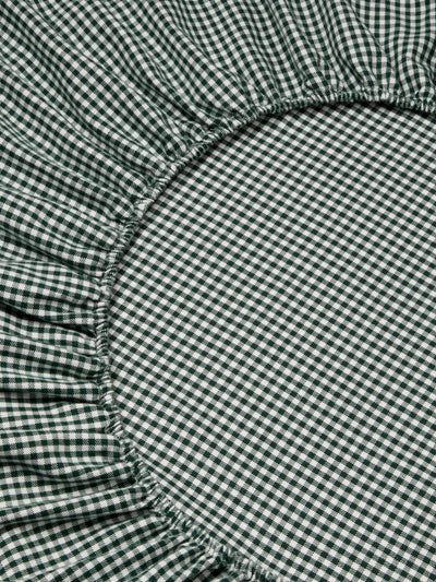 Close-up of a green and white gingham fabric with a gathered ruffled edge, showing the textile pattern and elasticized seam detail.
