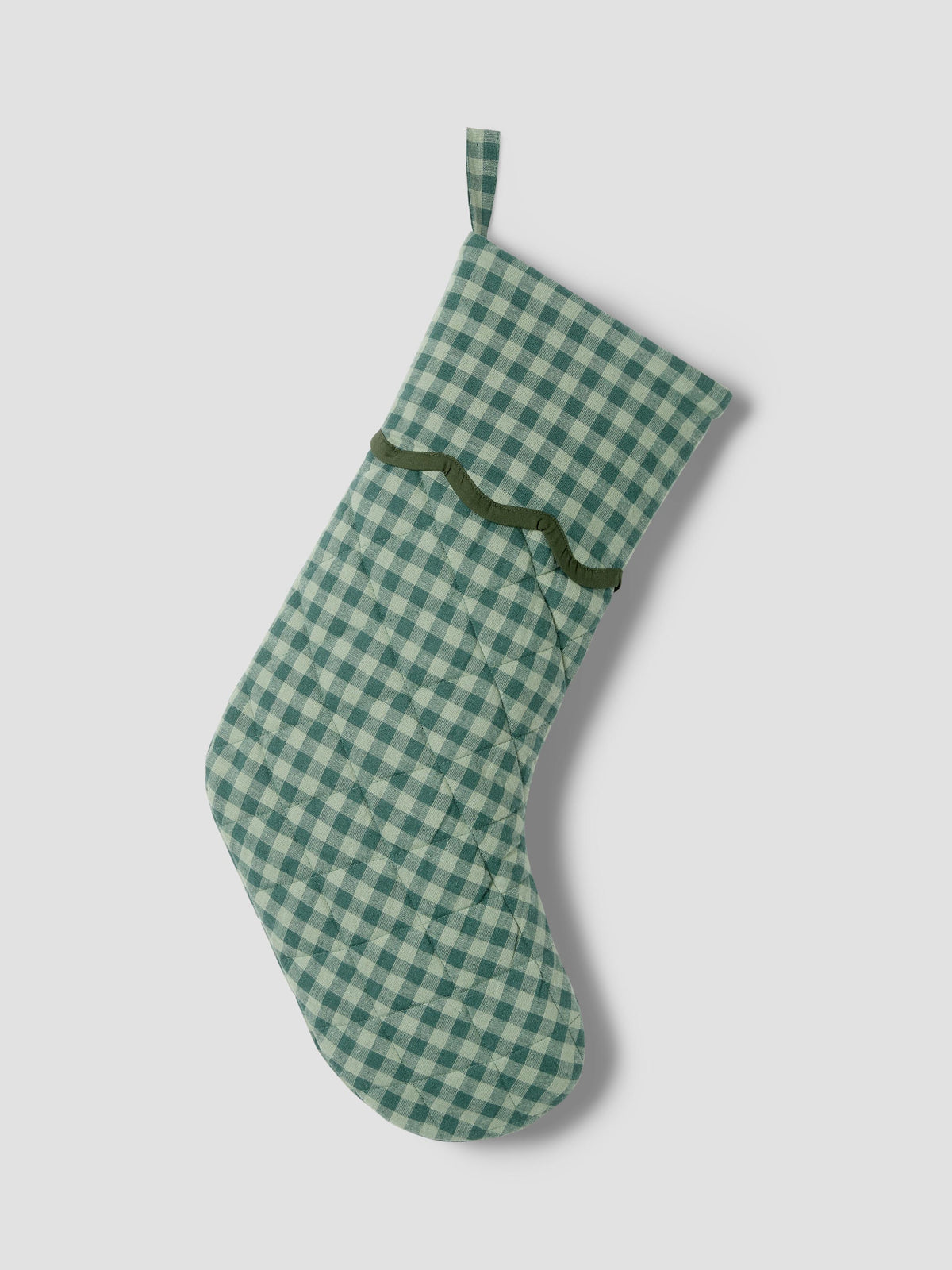 A green and white gingham patterned Christmas stocking with a dark green wavy trim detail, shown against a neutral light gray background.