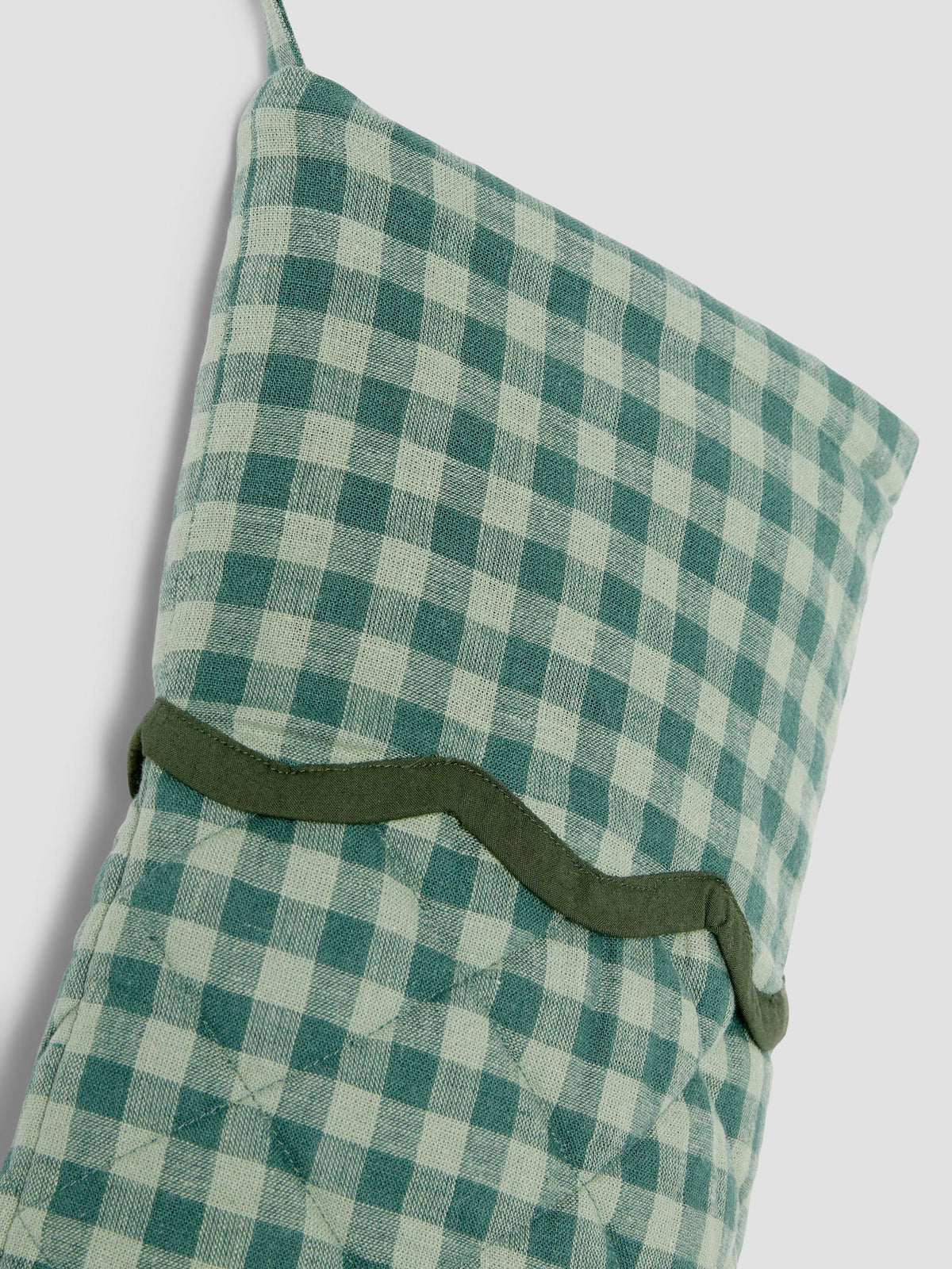 A close-up of a green and white gingham check stocking with a solid olive green wavy trim band across the middle, set against a plain light gray background.