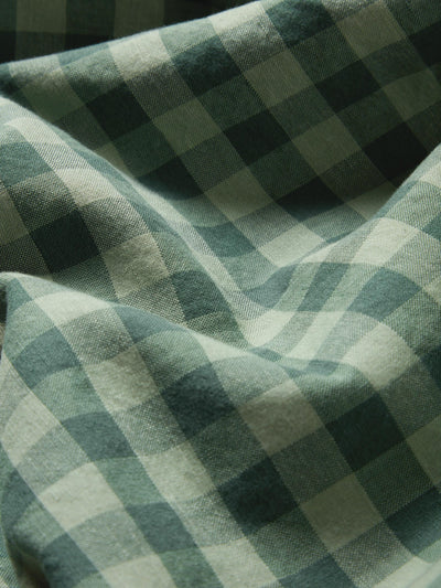 A close-up of draped fabric with a green and off-white gingham check pattern.