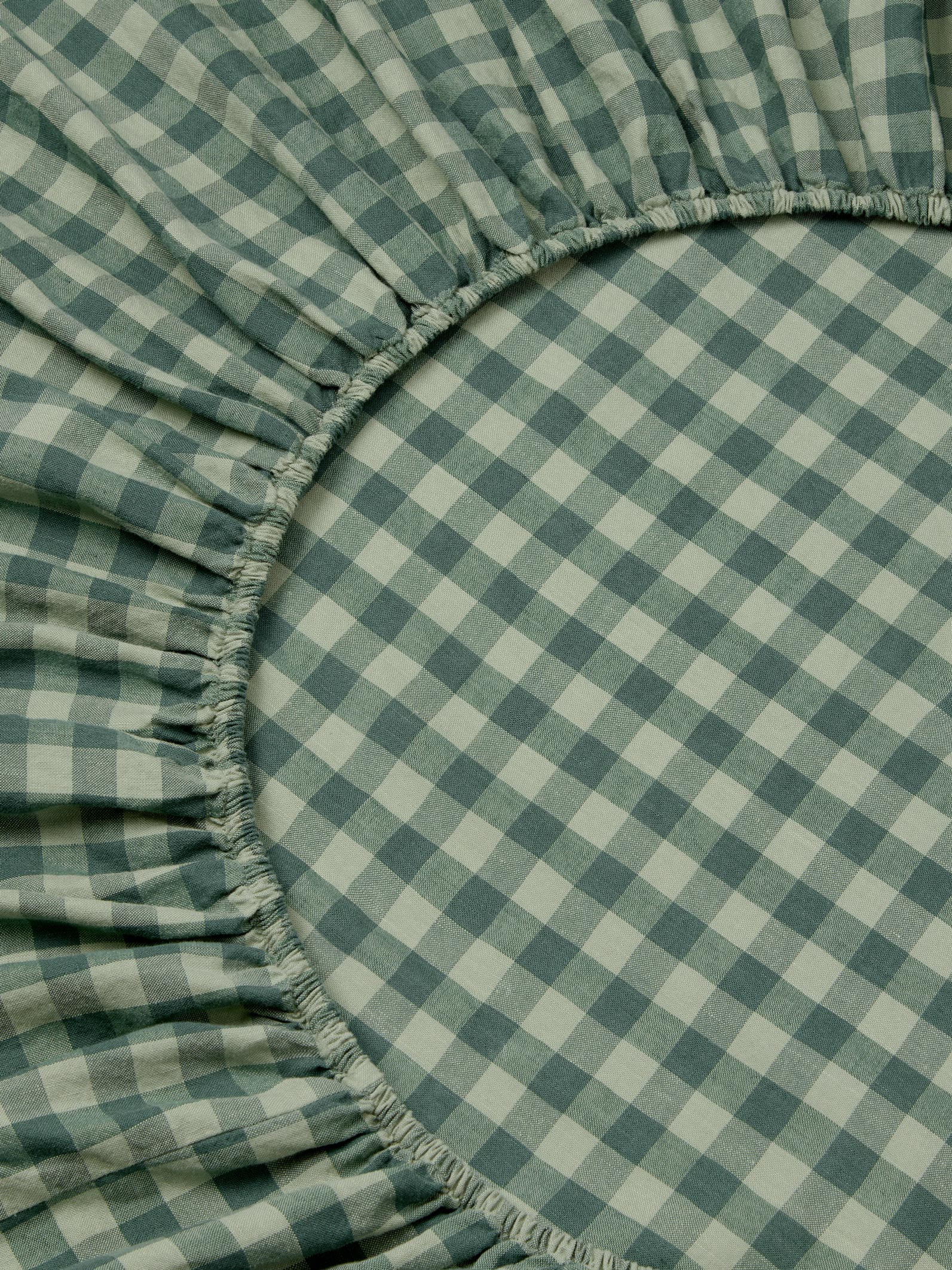 A close-up of a green and white gingham checkered fitted sheet with gathered elasticized edges