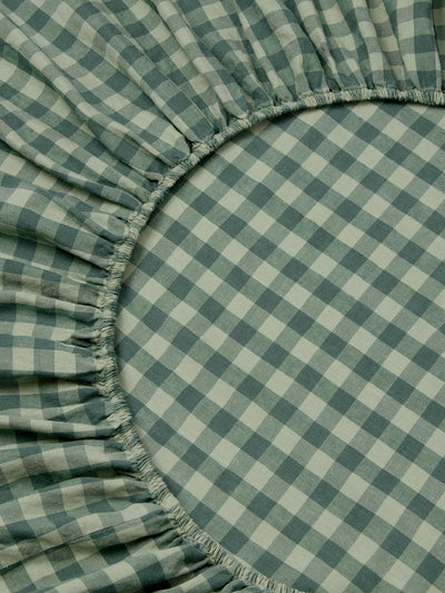 A close-up of a green and white gingham checkered fitted sheet with gathered elasticized edges