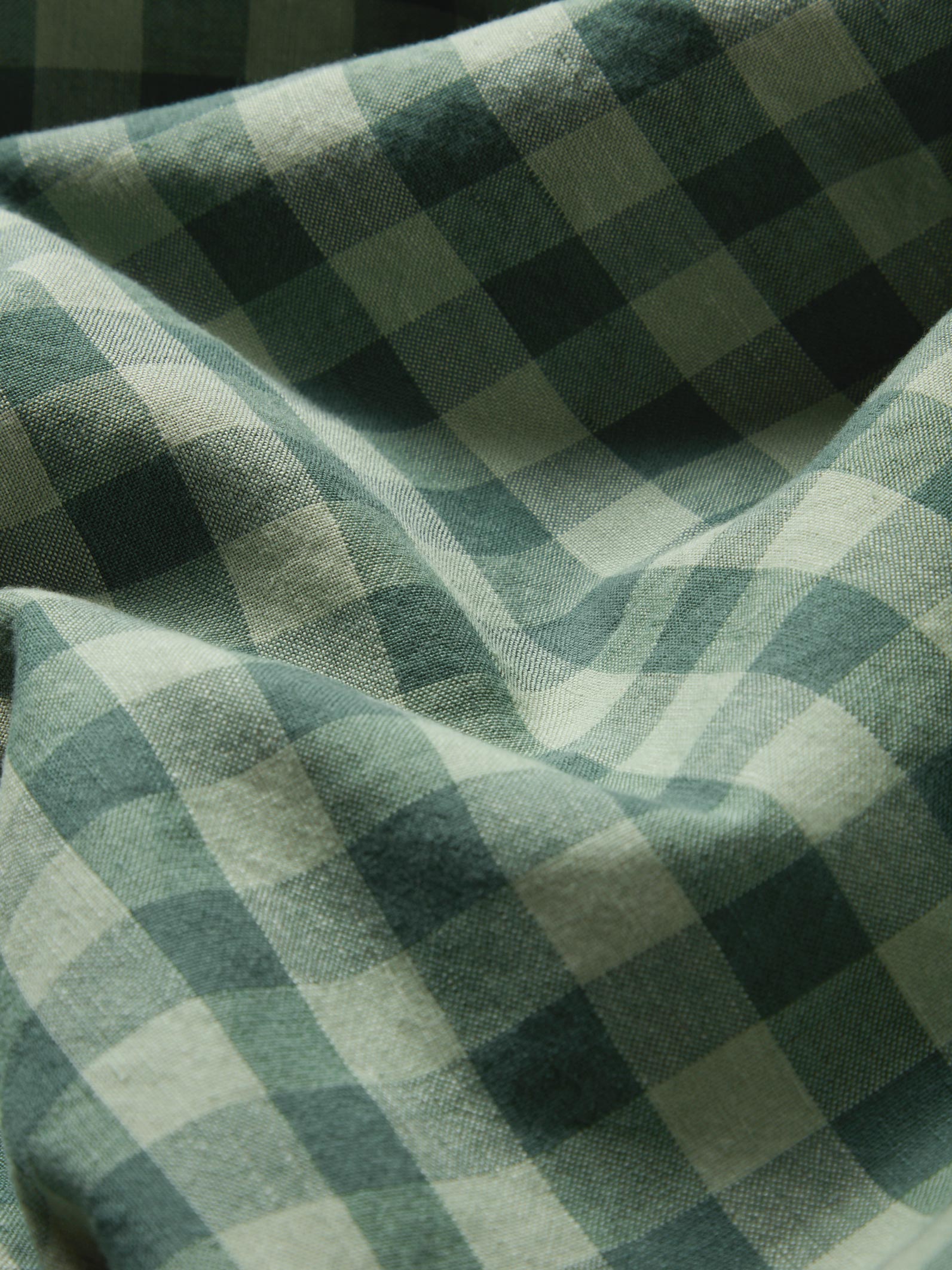 A close-up of draped fabric with a green and off-white gingham check pattern.