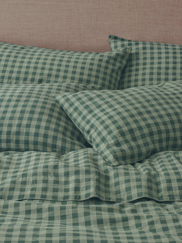 Green and white gingham check bedding set including two pillowcases and a duvet cover, styled on a bed against a textured pink headboard.