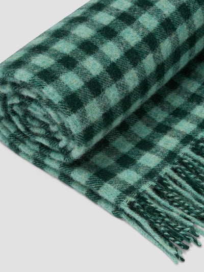 A green gingham blanket rolled up on a light grey background