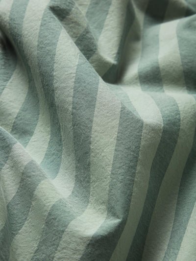 A close-up of draped fabric with a soft vertical stripe pattern in muted sage green and off-white.