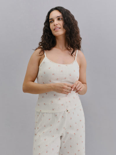 A woman modeling a ribbed knit two-piece pajama set with a small pink floral print, featuring a camisole top and matching pants, against a solid gray studio background.