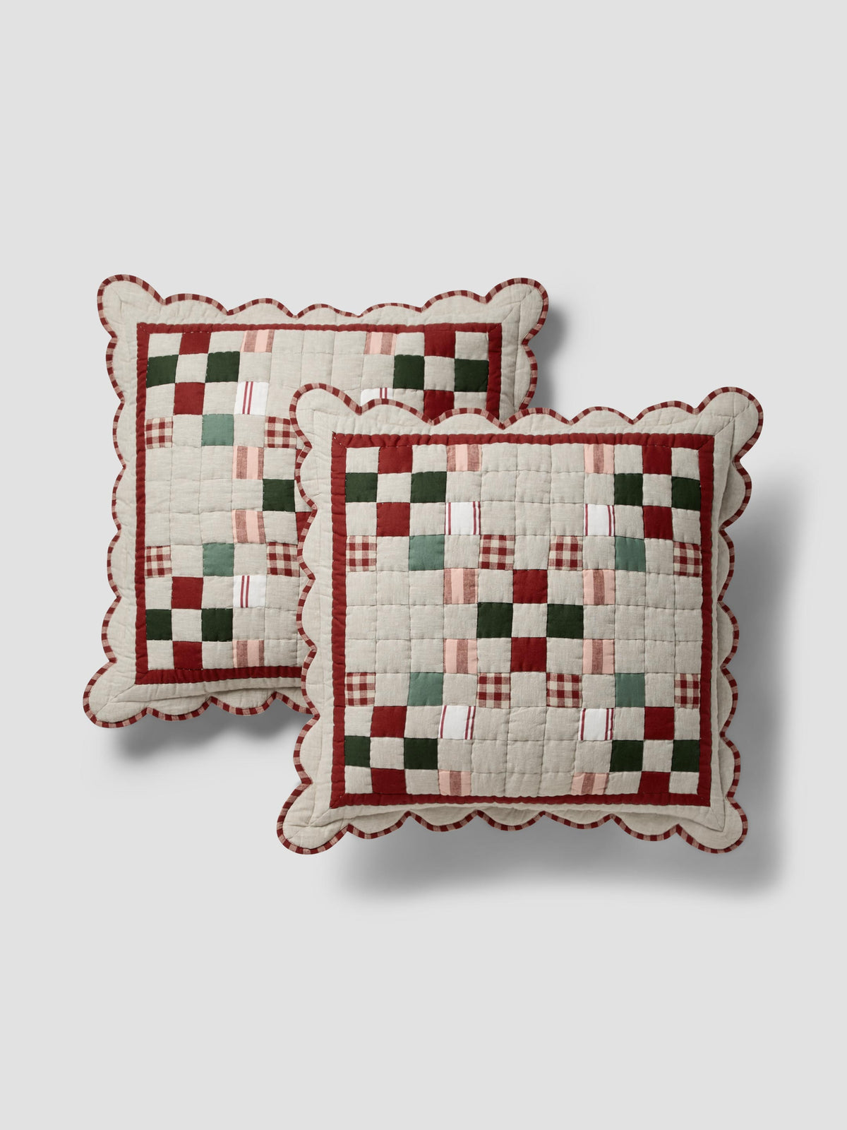 Two square quilted throw pillows with scalloped edges, featuring a rustic patchwork design in cream, burgundy, green, and pink on a light gray background.