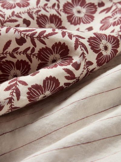 Close-up of a cream-colored fabric with a dark burgundy floral block print on one side and fine vertical burgundy stripes on the other.