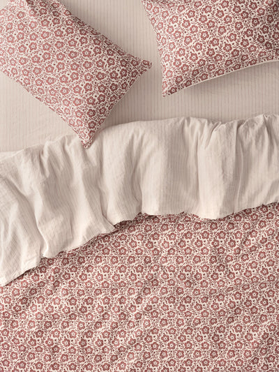 A close-up of a bedding set featuring a dusty rose and cream floral pattern on the duvet cover and pillowcases, with a solid cream ruffled pillowcase and sheet.