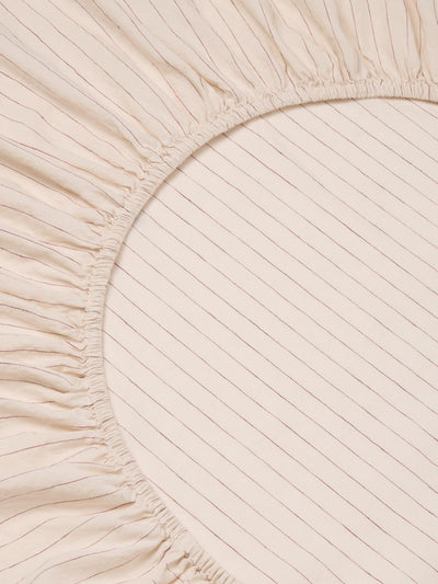 Close-up of a light beige or cream-colored fabric with a fine vertical stripe pattern and a gathered elasticized edge.