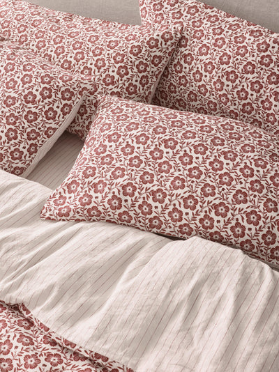 A close-up of a made bed with cream ribbed bedding and multiple pillows featuring a dusty rose floral pattern.