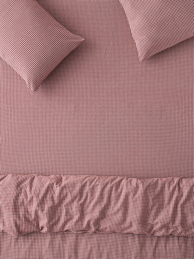 Overhead of a bed featuring two pillows, a fitted sheet and a duvet cover  with a red and white gingham check pattern.