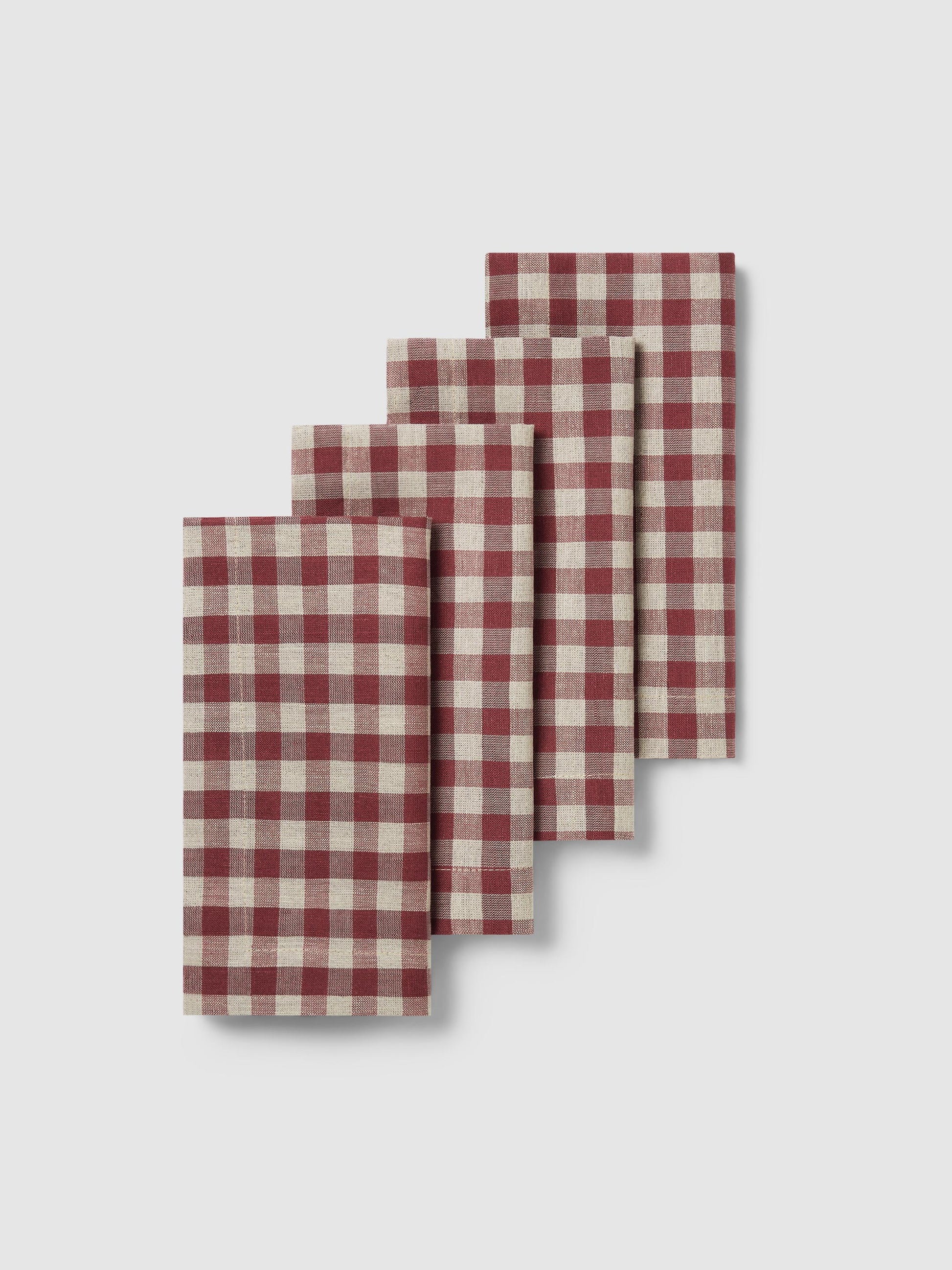 Four folded rectangular napkins with a red and cream gingham check pattern, arranged in a staggered stack on a light gray background.