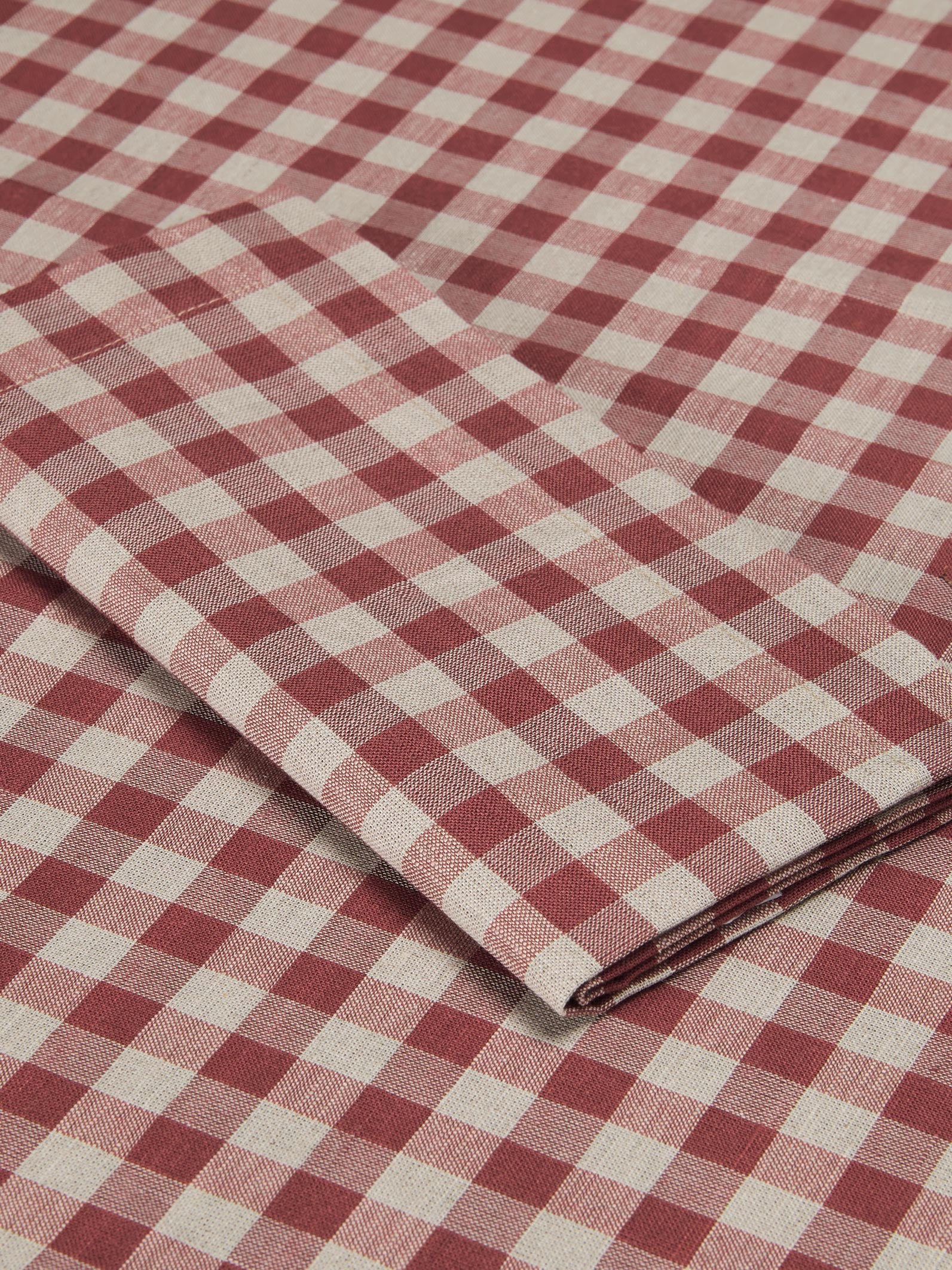 A close-up of folded and flat-laid red and off-white gingham checkered fabric, showing its woven texture and pattern.