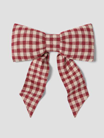 A red and cream gingham check bow accessory, photographed flat against a neutral light gray background.
