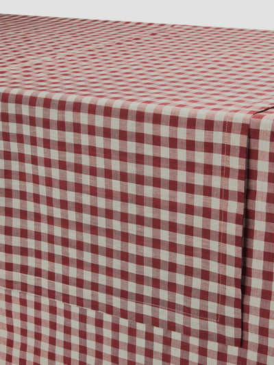 A close-up of a red and white gingham checkered tablecloth draped over a table, showing the fabric texture and pattern.
