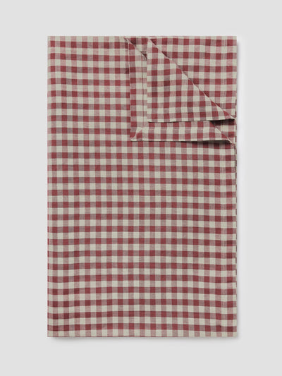 A folded checkered table linen in a muted red and oatmeal gingham pattern, shown against a neutral light gray background.