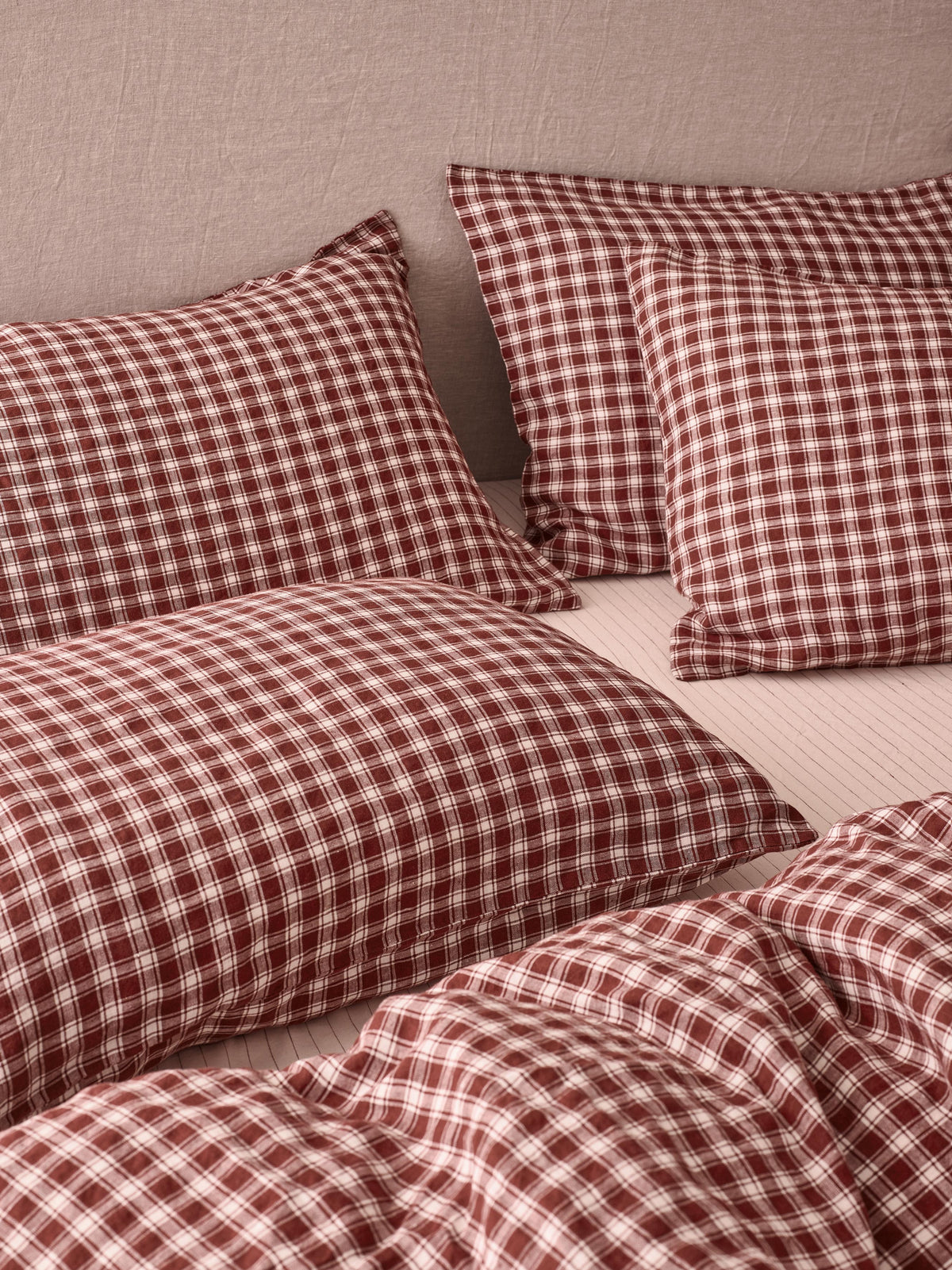 Red and white gingham check bedding set including two pillowcases and a duvet cover, styled on a bed against a neutral beige wall.