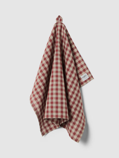 A white and rhubarb checkered tea towel hanging up on a light grey background.