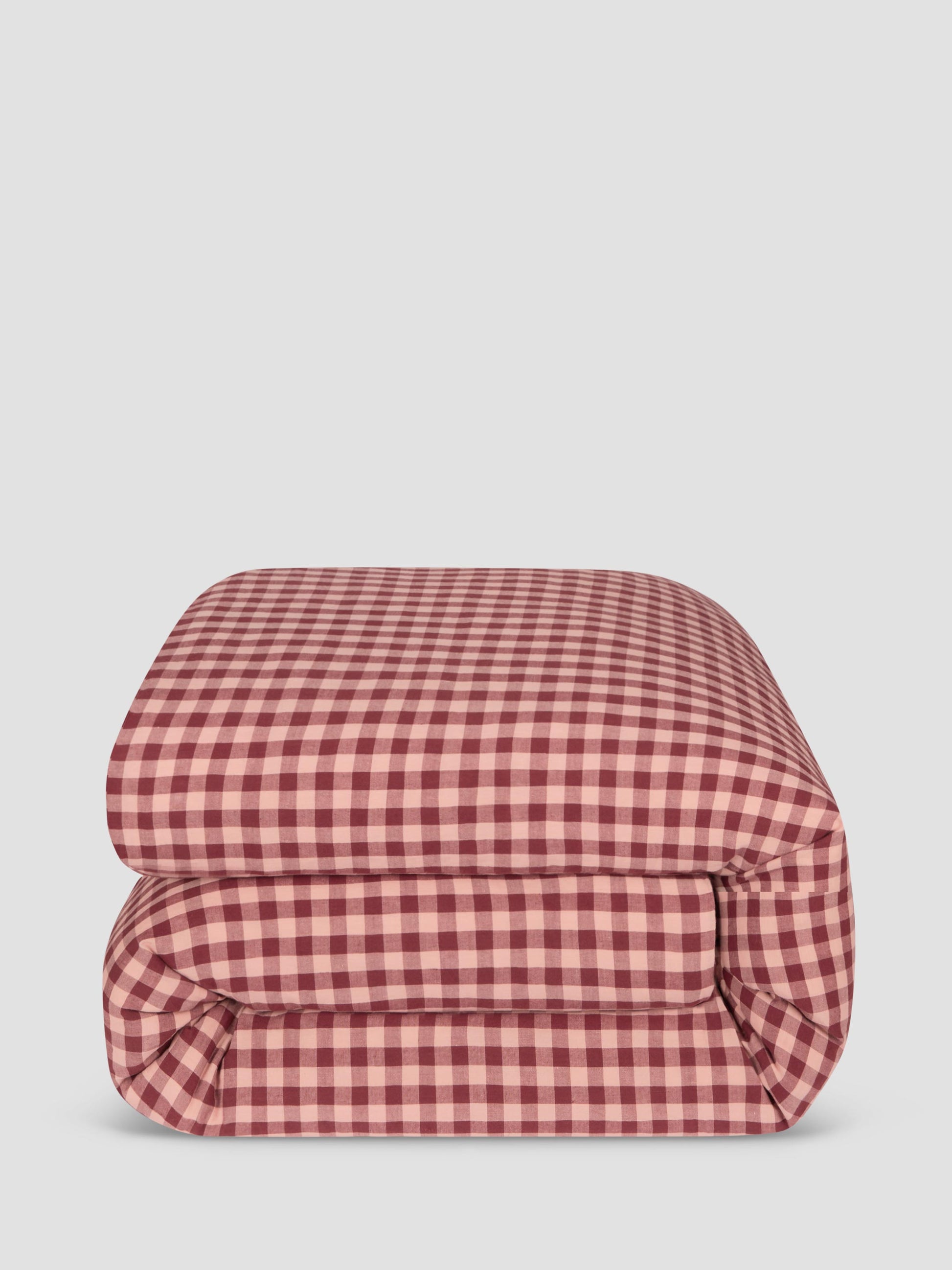 A folded comforter, featuring a classic red and white gingham check pattern, set against a solid light gray background.