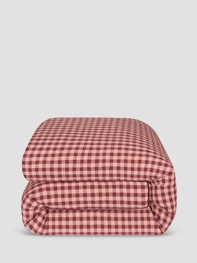 A folded comforter, featuring a classic red and white gingham check pattern, set against a solid light gray background.