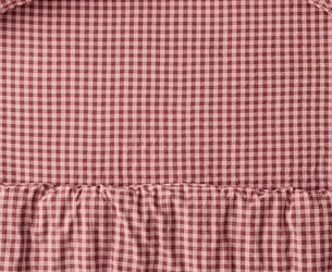 A close-up of a red and white gingham check bedding set with a ruffled hem and matching pillowcases.