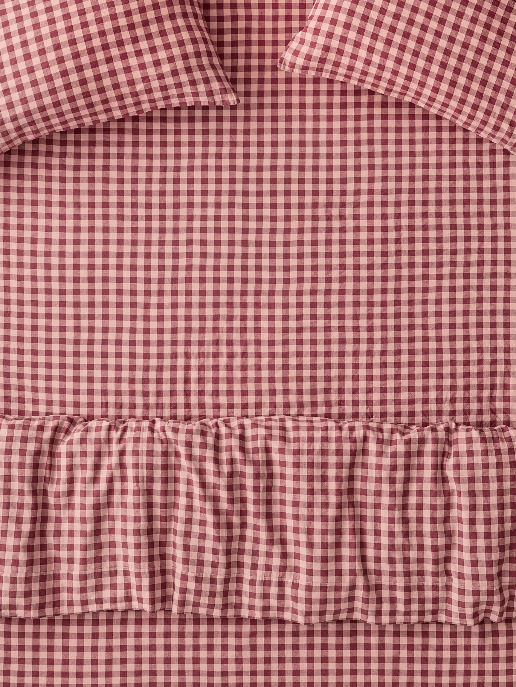 A close-up of a red and white gingham check bedding set with a ruffled hem and matching pillowcases.
