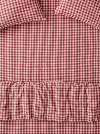 A close-up of a red and white gingham check bedding set with a ruffled hem and matching pillowcases.