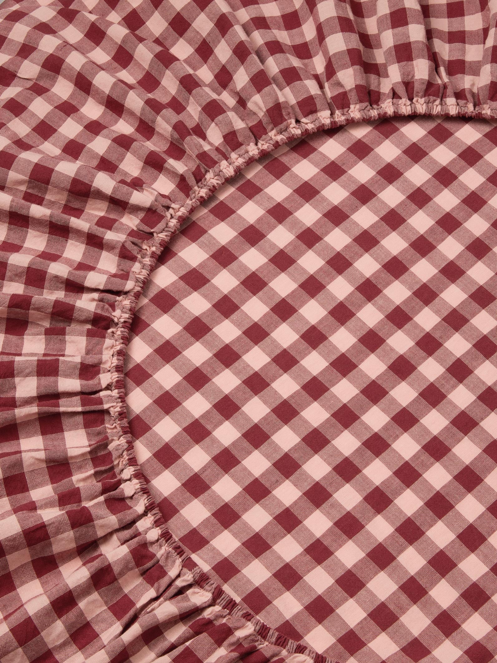 A close-up of a red and white gingham checkered sheet with a gathered elasticized edge.